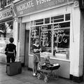 Two women, one with a pram and young child, the other with a suitcase, stand outside a fishmongers in Highgate Image preview